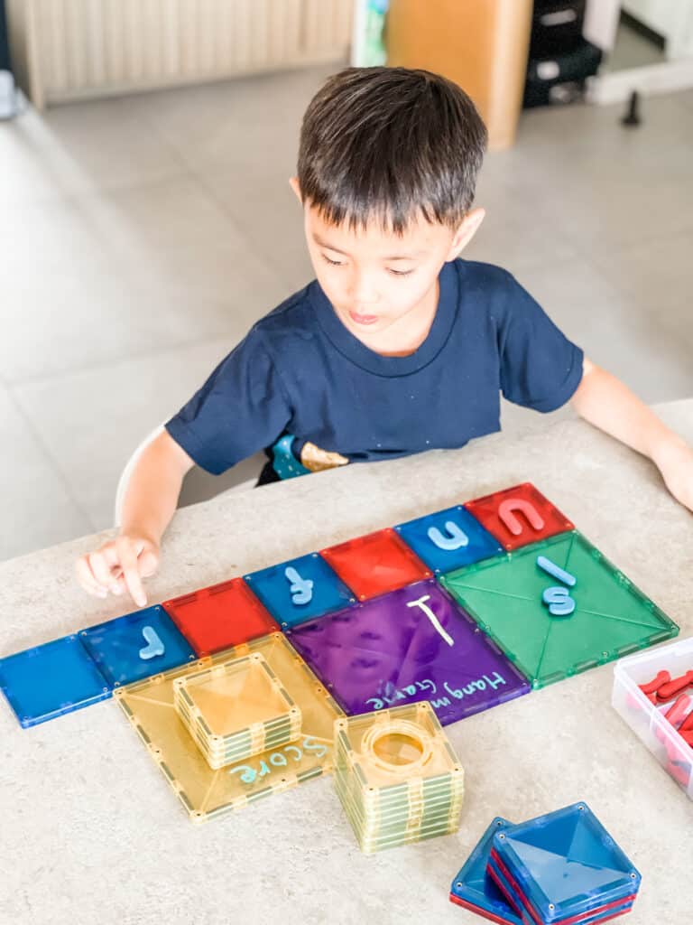 Child using Connetix to play hangman. 3 large tiles are used to record the hangman game, letter guess, and keep score. A row of standard squares are used to track the word being guessed.